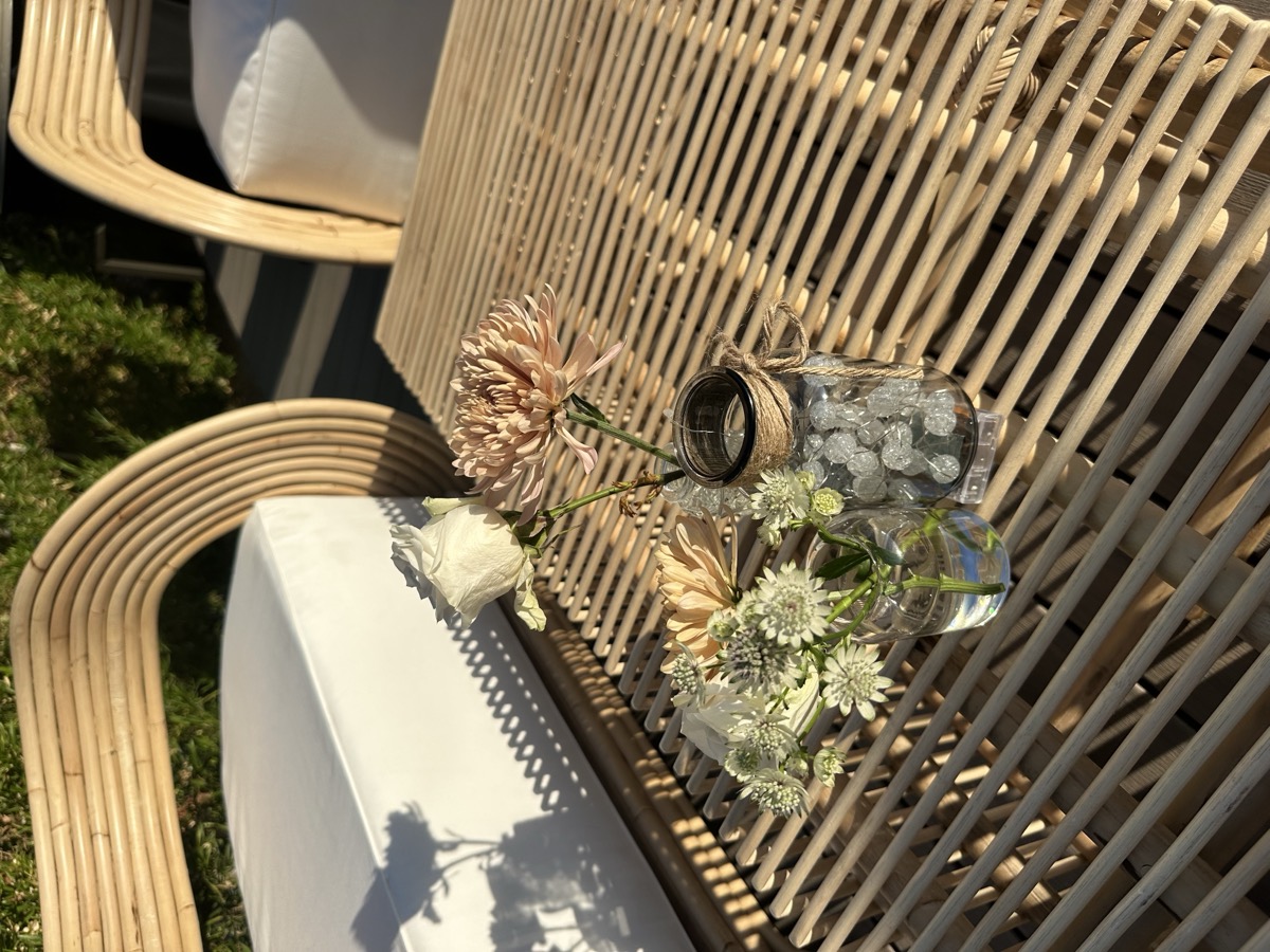 Bud vases of roses and chrysanthemums on a woven rattan table in late afternoon light
